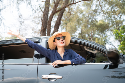 A joyful traveler is feeling the coastal breeze as she drives her SUV. Dressed in a chic sun hat and sunglasses and the calm ocean backdrop completing this perfect getaway
