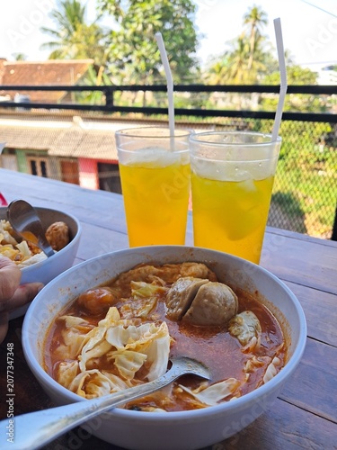Spicy Indonesian Meatball Soup with Fresh Cabbage and Iced Drinks on Outdoor Restaurant Table