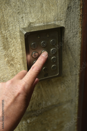 Closeup of a finger pressing a security keypad at the entrance of an apartment building. Access control system for residential security and protected entry.