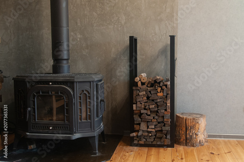 Black cast iron wood stove with firewood stack and log stump in modern interior