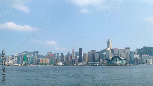 Modern skyscrapers and corporate towers along the waterfront of Victoria Harbour in Hong Kong under a blue sky.