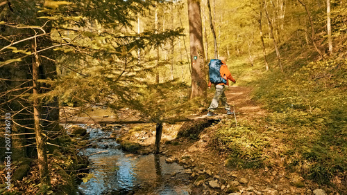 Obraz na plátně A hiker navigates a forest trail beside a flowing stream, surrounded by autumn foliage