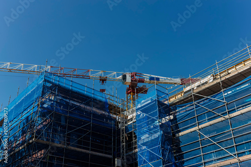 Bright blue safety netting wraps scaffolding on a building under construction beneath a tower crane.
