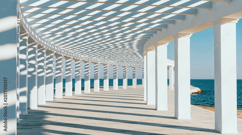 Fototapeta premium Architectural pergola framing ocean, creating repeating patterns of light and shadow on a curved pathway under a clear blue sky