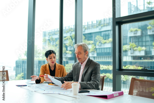 Obraz na płótnie Senior executive reviews financial reports with young business professional during corporate meeting inside modern office