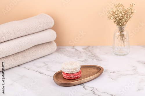 Eco solid shampoos stacked on a wooden tray with beige towels and a vase with dried flowers. Peach background and marble surface. Horizontal image with copy space