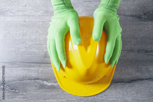 Photos Hands in green protective gloves holding yellow hard hat