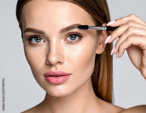 Retrato en primer plano de una mujer joven modelo con una piel facial suave y saludable maquillándose las cejas con un lápiz cepillo de cejas
