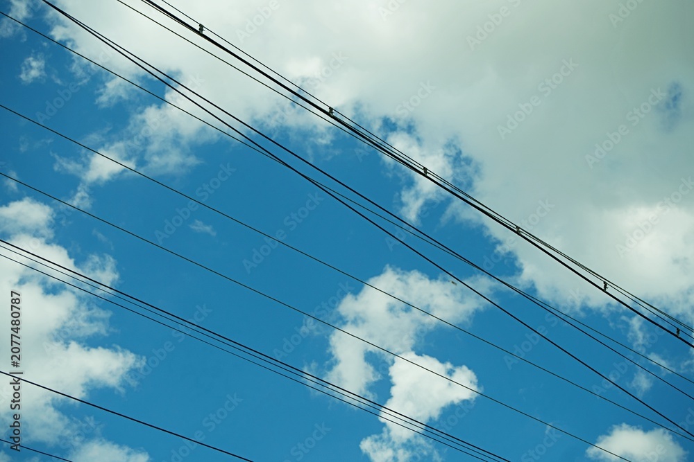 Fototapeta premium Power lines against a beautiful blue sky with white fluffy clouds on a sunny day