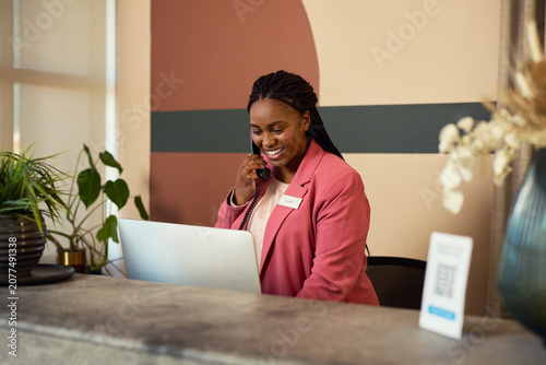 African receptionist working while talking on phone at desk