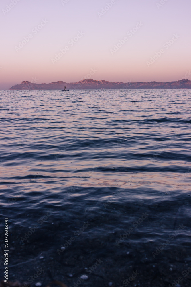 Obraz premium Calm sea in northern Mallorca at sunset with a lone person paddleboarding 