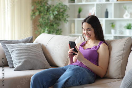 Happy young woman using smartphone sitting on a couch