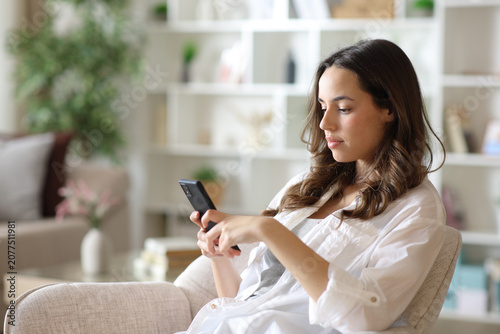 Serious woman using a cell phone sitting on armchair