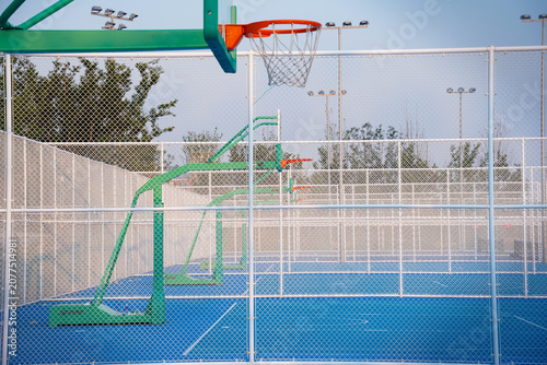 Obraz na plátně Empty outdoor basketball court enclosed by a fence, with multiple green basketball hoops and blue playing surface