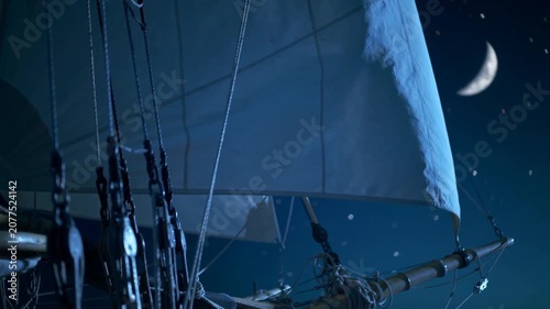 Billowing foresail and nearby rigging catching wind under crescent moon, powering vessel forward