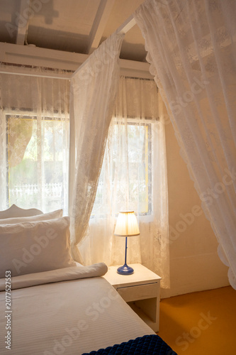 Konstfotografi Close-up of a white canopy bed with pillows and bedside lamps in a white-themed cottage bedroom, showcasing elegant furnishings and a clean, contemporary interior