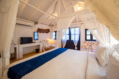 Bild auf Leinwand White-themed cottage house interior featuring a canopy bed with bedside lamps, a bed bench, sofa, and TV, showcasing a bright, elegant, and contemporary bedroom with a clean aesthetic