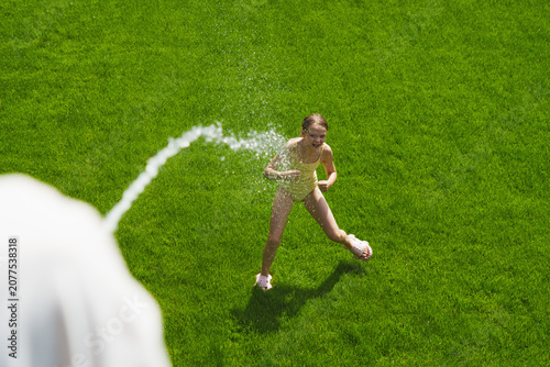 A cheerful child plays with water sprinklers in the garden during the summer. Creatively watering the garden—with fun and high spirits. An authentic, real little girl.