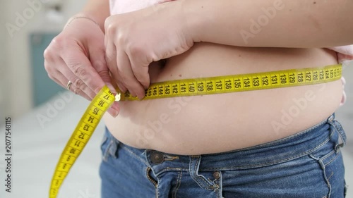 Close-up of a person measuring waist circumference with a measuring tape to monitor body fat, obesity, weight loss, fitness progress, and healthy lifestyle goals.