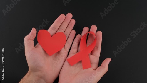 Hands holding a red heart and red awareness ribbon symbolizing HIV/AIDS awareness, compassion, healthcare support, disease prevention, global health campaigns, and patient advocacy.