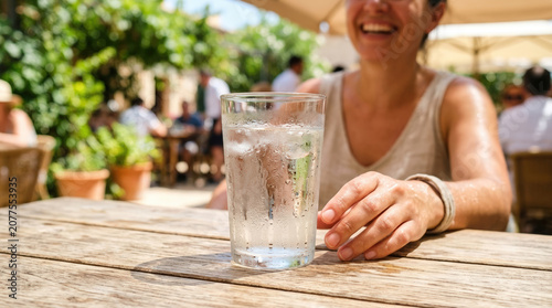 Cold glass of ice water with condensation on a wooden table. Refreshing drink at an outdoor cafe on a hot summer day. Hydration and coping with sweltering heat concept