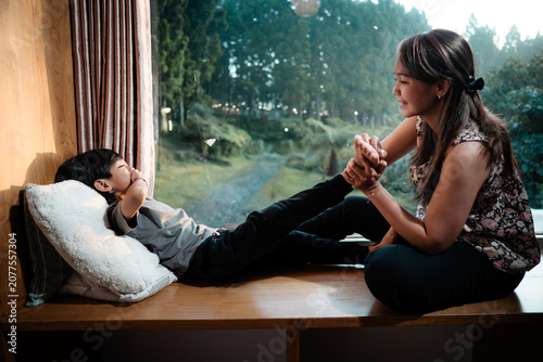 Foto A mother lovingly playing and tickling the feet of her happy young son while sitting by a large window with a scenic outdoor view