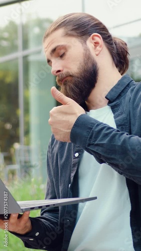 Business man walking along a city street while conducting a video call on her laptop. Corporate professional, urban environment, modern communication technology, online work, digital lifestyle.
