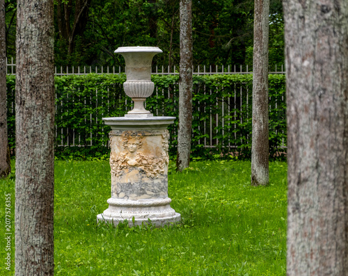 An antique vase on a pedestal in a park on a summer day.