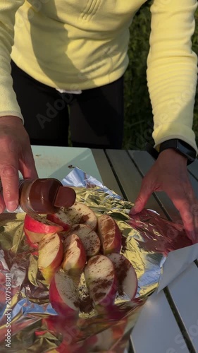 Close up of mature woman sprinkling ground cinnamon spice over chopped apples at campsite.