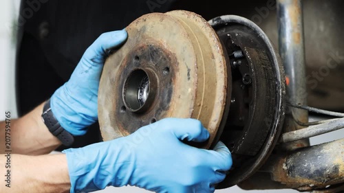 A car mechanic wearing gloves removes a brake drum from a car wheel for inspection and repair.