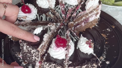 Woman's hand takes a slice of chocolate cake with cherry and whipped cream from a tray