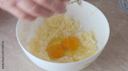 Hand cracks an egg into a white bowl with butter mixture while preparing dough