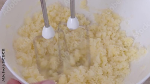 Mixing dough with a hand mixer in a white bowl in close up