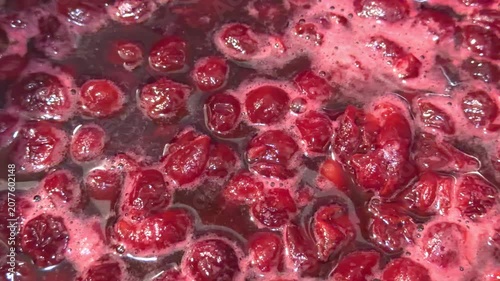 Boiling cherry jam with berries in dark syrup and foam in close up