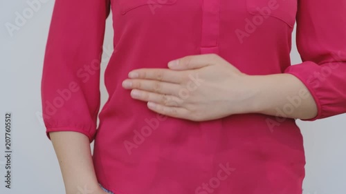 Young woman holding her abdomen due to stomach pain, digestive discomfort, cramps, or gastrointestinal problems while sitting at home. Healthcare and wellness concept.