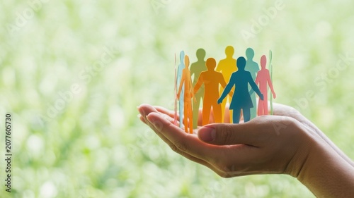 Human hands holding a circle of colorful paper cutout people representing community support and social responsibility for global diversity and inclusion
