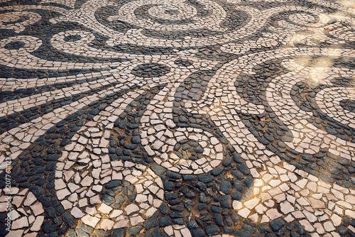 Pattern of stones on  sidewalk in  city. daylight hours showing artistic design. sidewalk features a design made of various stones arranged in curves and swirls. artwork  pavement patterns during day