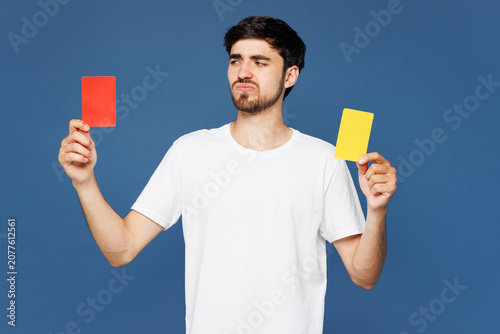 Foto Young sad man fan wear white t-shirt cheer up support football sport team hold soccer ball, red or yellow card propose player retire from field watch tv live stream isolated on plain blue background