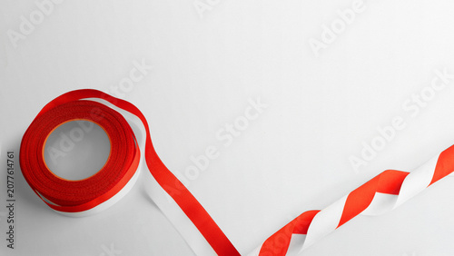 Tableau sur toile A roll of red and white warning hazard tape unrolling on a plain white surface with space for text