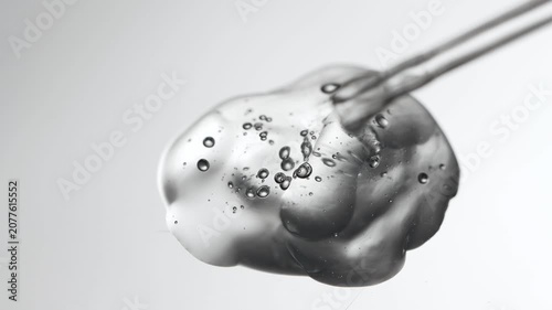 Drop of liquid transparent texture close-up with pipette close-up on gray background.