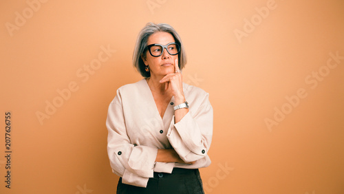 Tableau sur toile Mature woman with glasses and grey hair standing against a plain background, con
