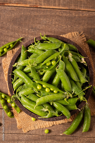 Fresh green peas and pods in a bowl on wooden table. Vegetable healthy food.  