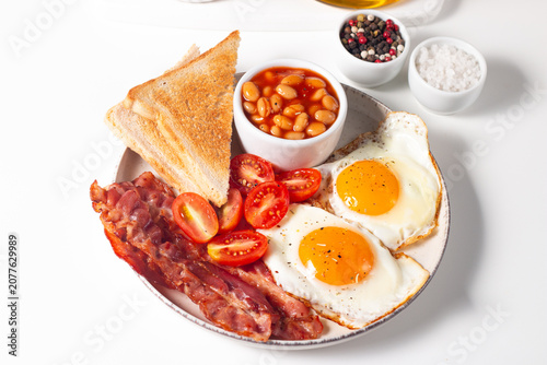 Delicious traditional English breakfast with fried eggs, beans, bacon, tomatoes and toasts