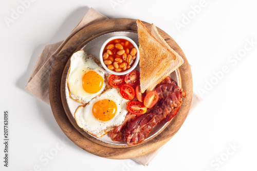 Delicious traditional English breakfast with fried eggs, beans, bacon, tomatoes and toasts