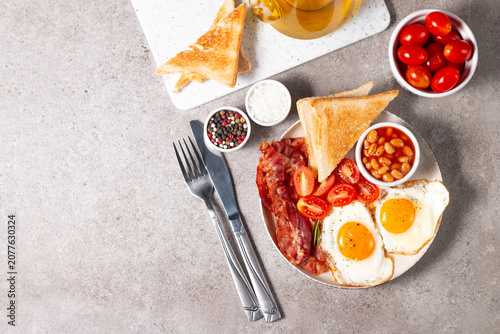 Delicious traditional English breakfast with fried eggs, beans, bacon, tomatoes and toasts