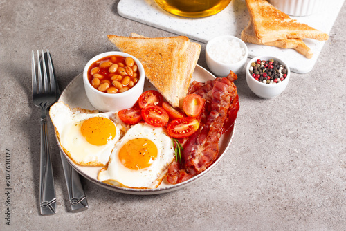 Delicious traditional English breakfast with fried eggs, beans, bacon, tomatoes and toasts