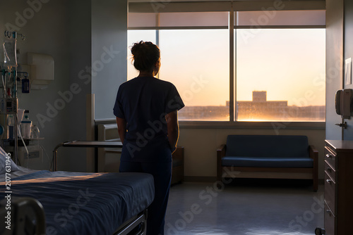 Lone nurse silhouetted by dawn in quiet hospital ward