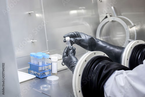 Scientist handling sample vial inside sealed glovebox isolator