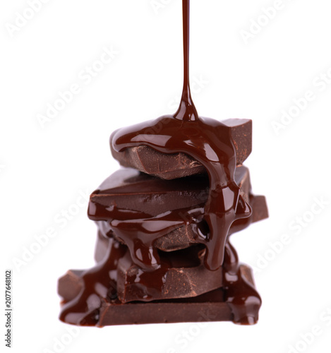 Liquid chocolate syrup pouring over a stack of chocolate pieces isolated on a white background. Clipping path.