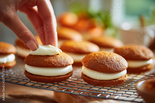 Hand applying frosting on carrot cake whoopie pies on rack